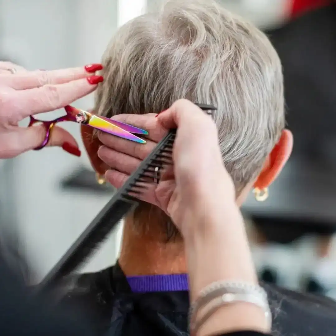 Hairdresser cutting short gray hair with scissors and comb.