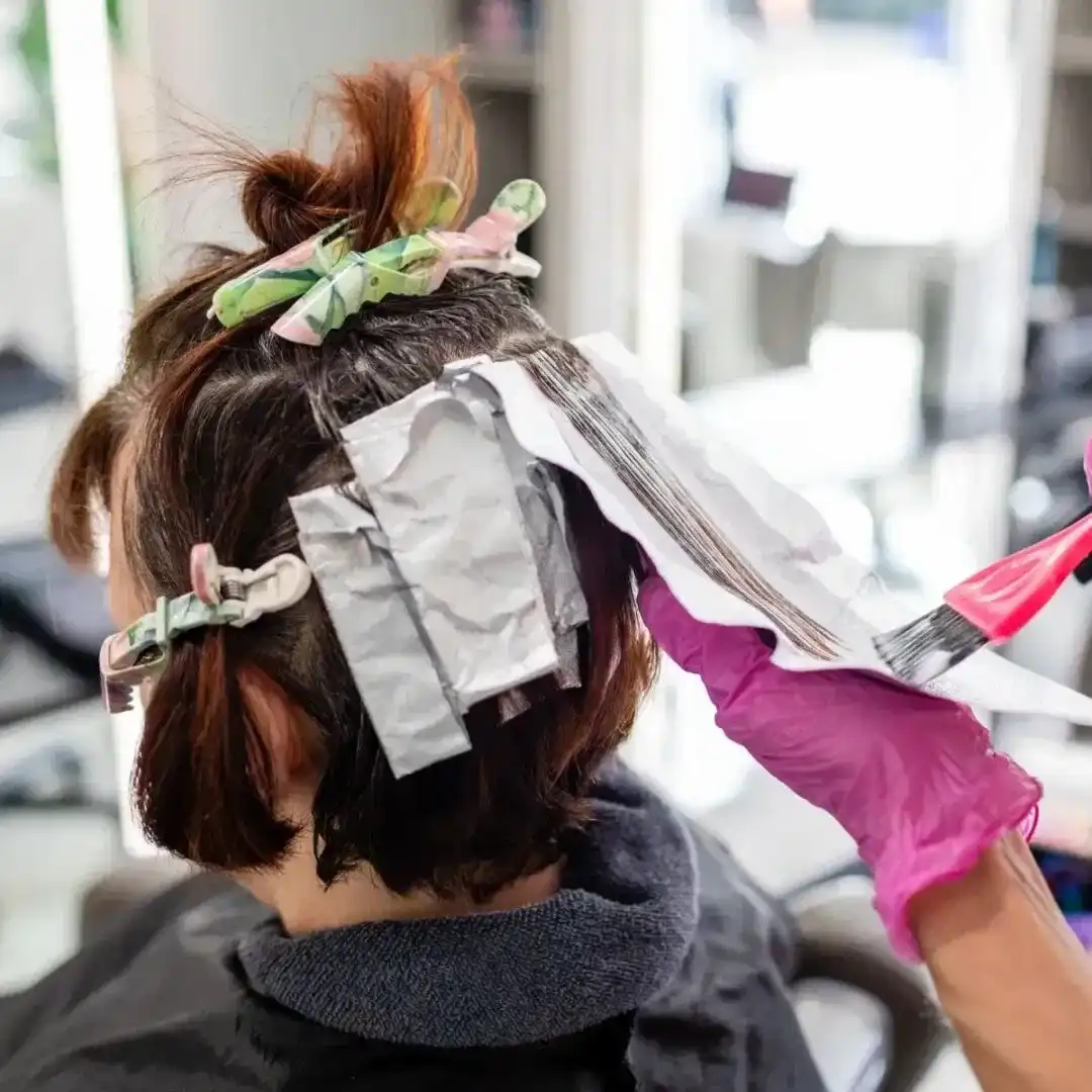 Hairdresser applying hair dye with foil and brush in salon.