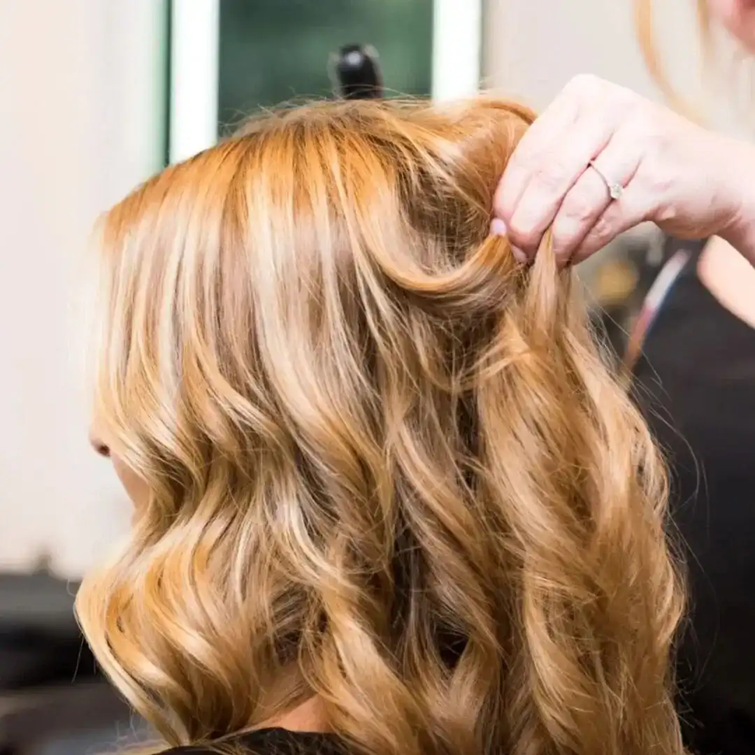 Hairstylist creating wavy blonde hairstyle with skillful hands in a salon.